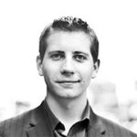 Portrait of a person in a suit, looking directly at the camera, against a blurred background.