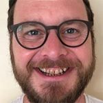 Man with glasses and a beard smiling at the camera.