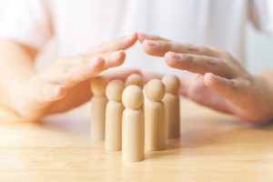 Hands are forming a protective gesture over a group of wooden figurines on a table.