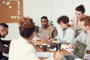 Man Wearing Brown Suit Jacket & People Sat Around Working