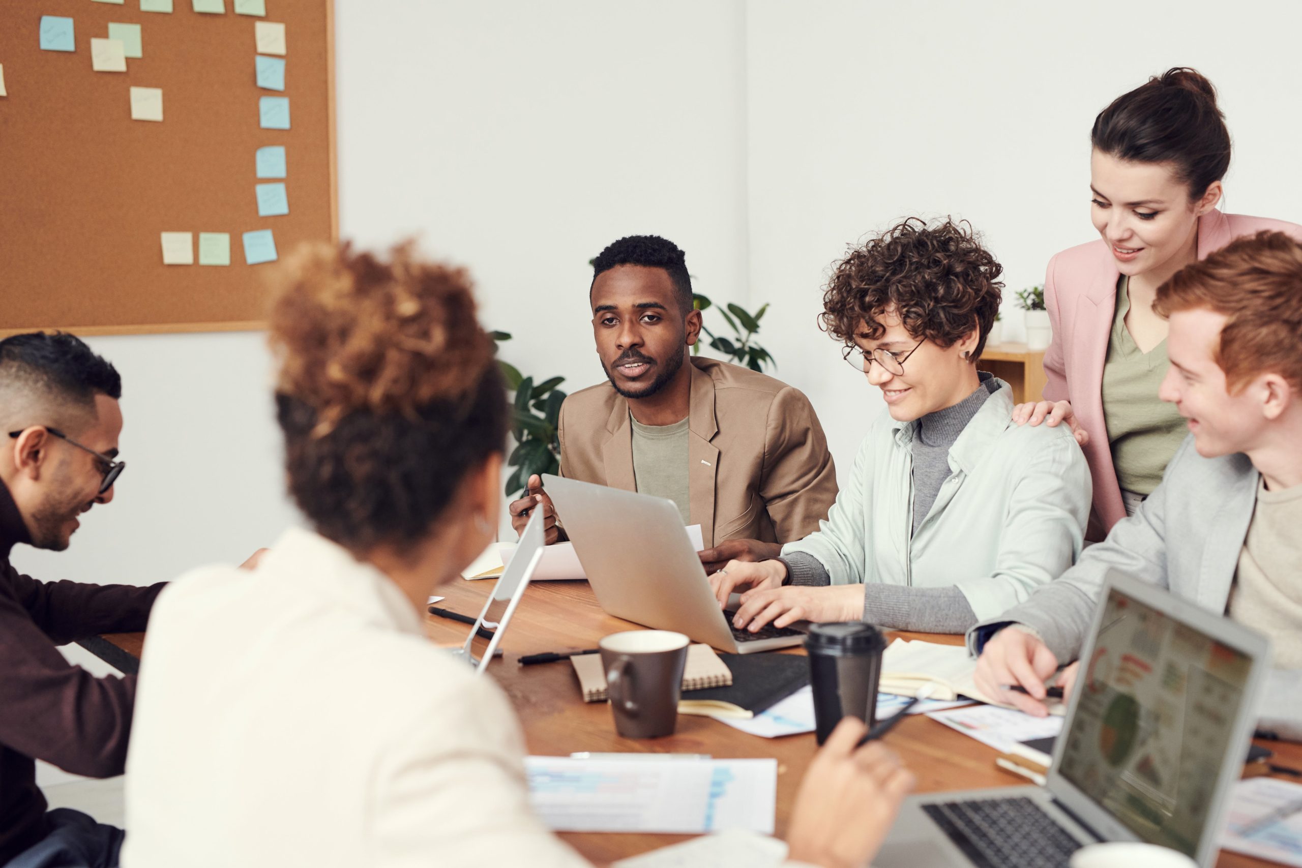 Man Wearing Brown Suit Jacket & People Sat Around Working