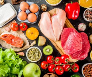 Assorted foods including chicken, beef, salmon, eggs, cheese, fruits, vegetables, seeds, and spices are artfully arranged on a dark surface—a perfect scene to explore how to check for food intolerance with these varied ingredients.