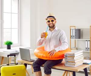 Smiling office worker wearing holiday accessories, sitting at desk with a drink and inflatable ring, symbolising taking time off under an annual leave policy