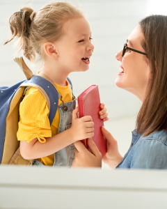 A smiling young girl wearing a backpack and holding a red book shares a joyful moment with her mother, highlighting the positive impact of benefits for working parents in supporting family life and education.